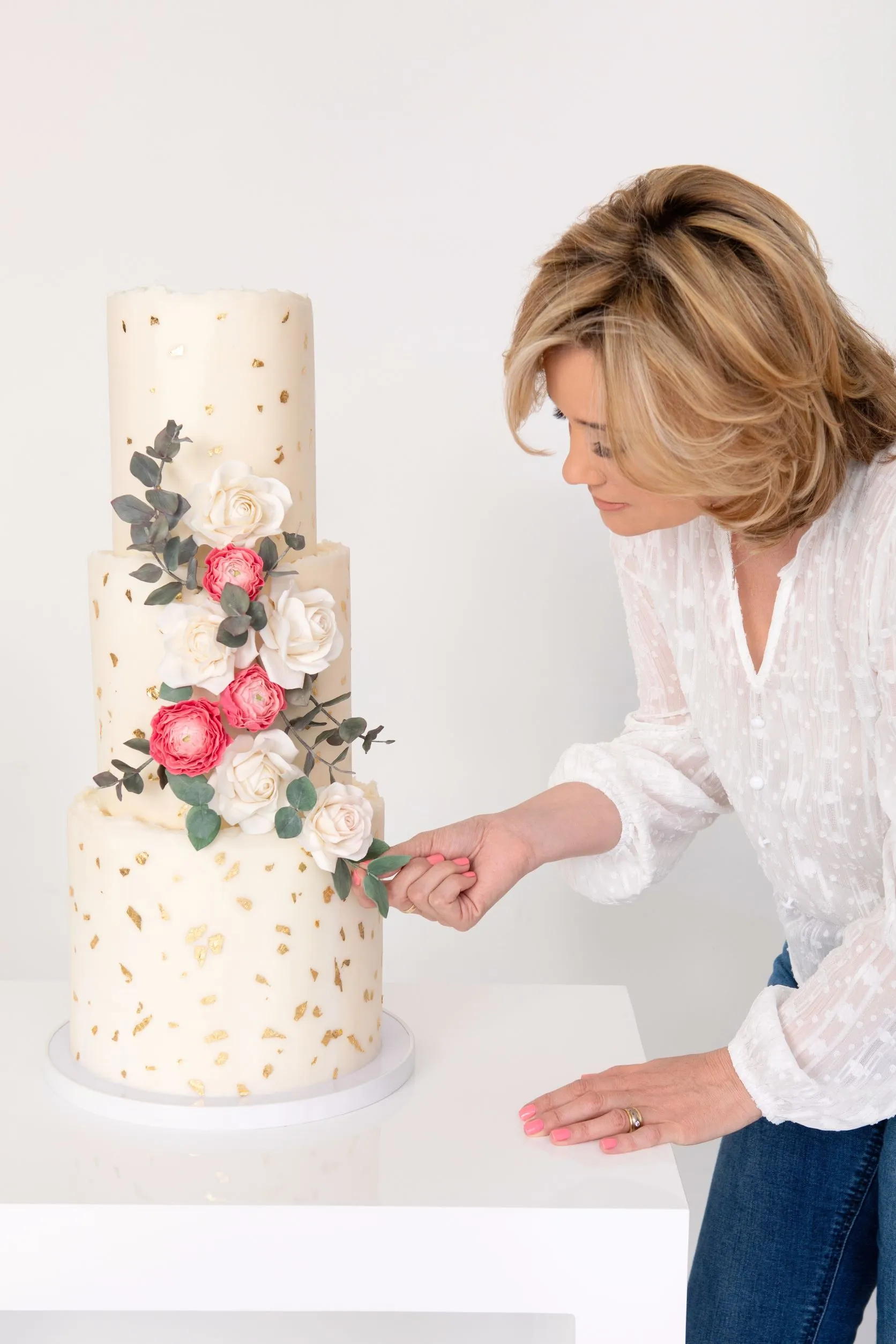 Grace Stevens arranging sugar roses on a three-tier white and gold-leaf wedding cake